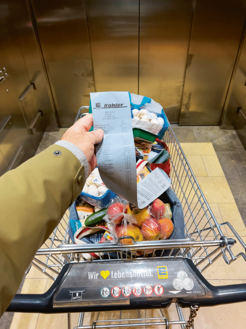 Kehl, Germany - March 13, 2022: POV male hand holding supermarket receipt from Edeka Supermarket in the elevator of a shopping center looking at the rised prices of products in the cart