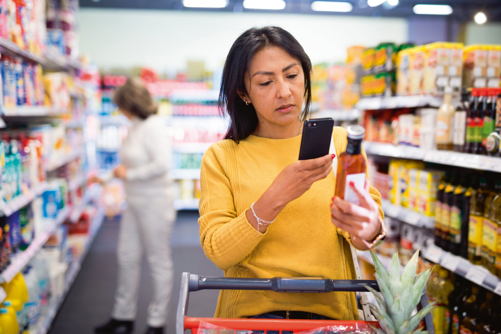 Latin american woman making purchases in grocery store, using smartphone to scan barcode of products. Modern shopping concept
